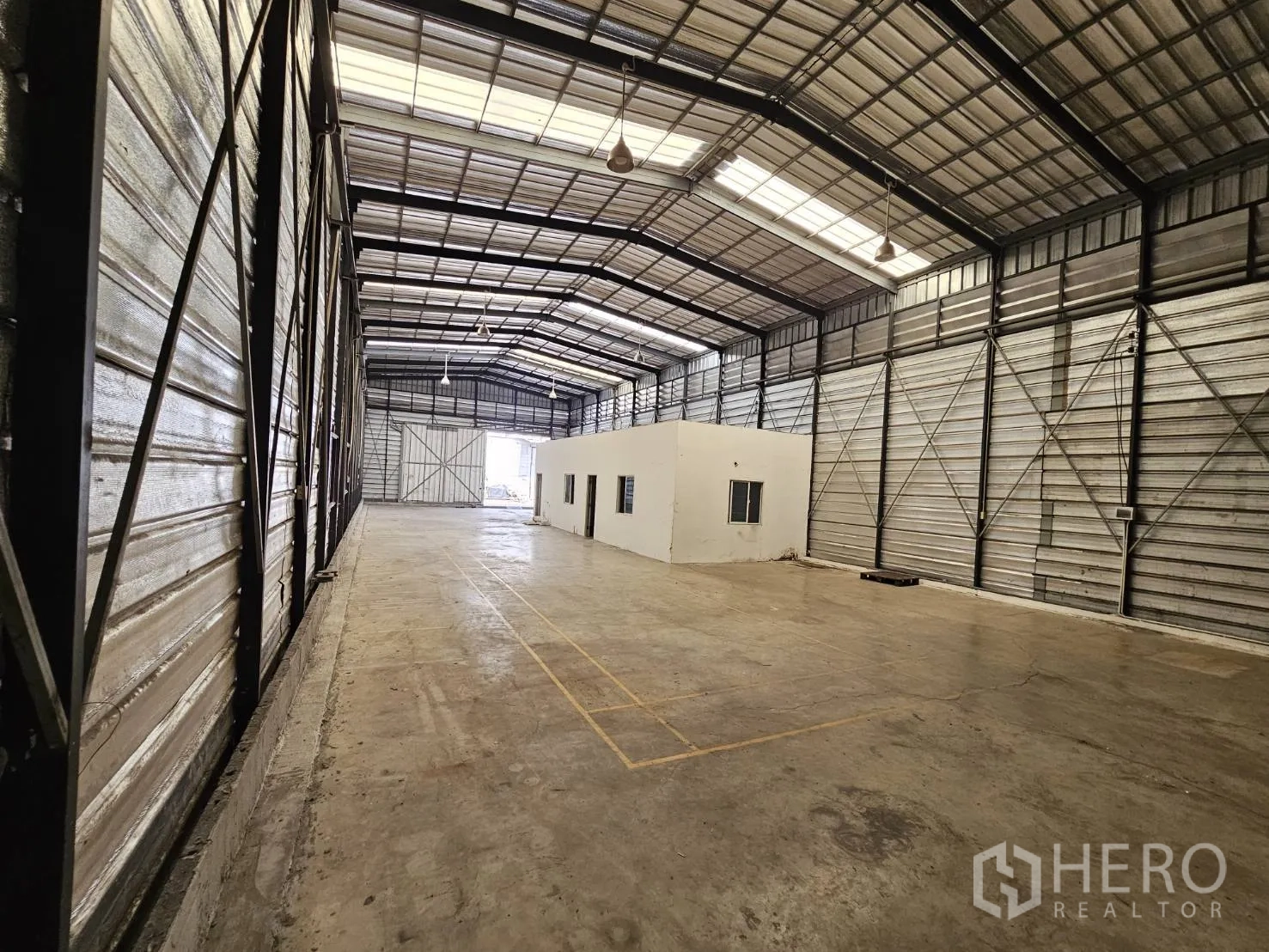 Warehouse for rent in Bang Phli, Samut Prakan - Long view of the warehouse showing central office unit, concrete floor, and a large sliding door.