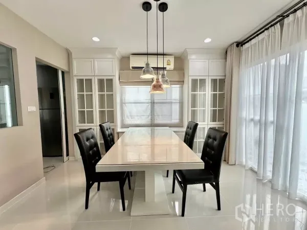 Detached House for rent in Bang Phli, Samut Prakan - Dining area with pendant lights, glass cabinetry and a large table beside wide windows.