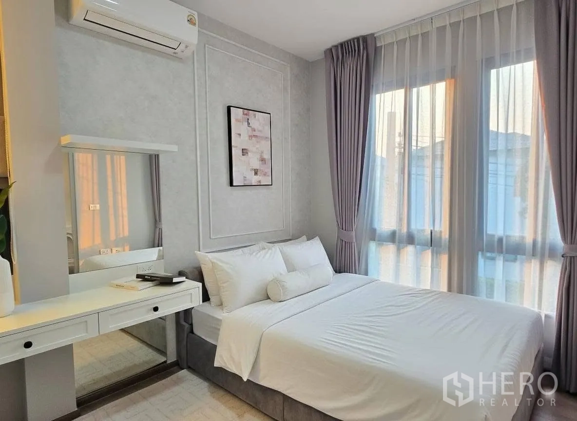Detached House for rent or sale in Bang Phli, Samut Prakan - Sunlit bedroom with large windows, sheer curtains, and a dressing table beside the bed.