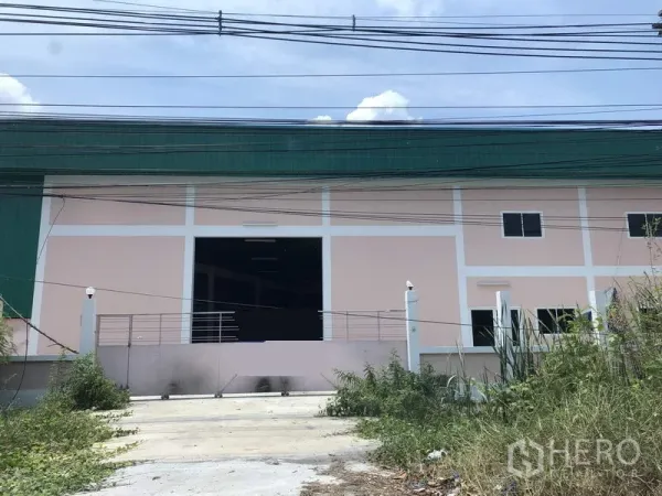 工厂 出租在Pathum Thani - Lat Lum Kaeo 工厂外观，粉红与绿色立面，宽大装卸入口、带门禁车道与路边电线。