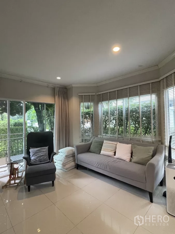 บ้าน ขายในMin Buri, Bangkok - ห้องนั่งเล่นสว่าง มีกระจกบานใหญ่รอบมุม โซฟาและเก้าอี้พักผ่อน เปิดมองสวน