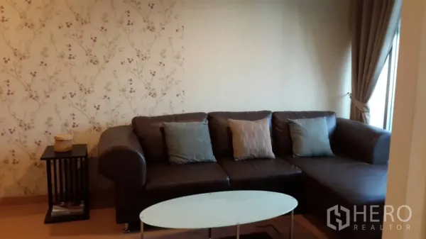 คอนโด ให้เช่าในWatthana, Bangkok - มุมนั่งเล่นอบอุ่น โซฟาหนังสีน้ำตาล โต๊ะกลางกระจก และวอลเปเปอร์ลายดอกไม้