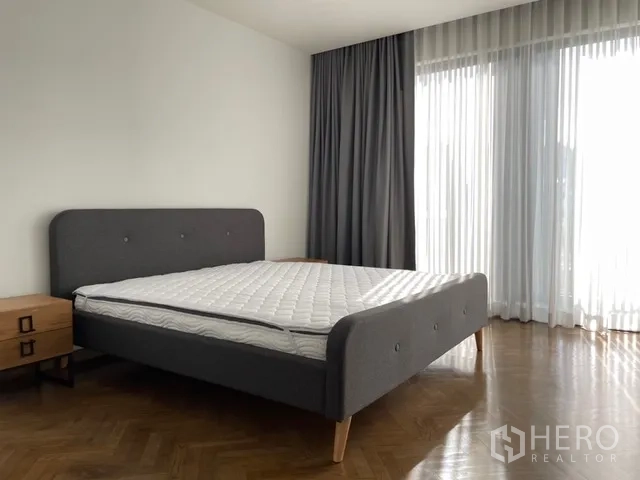 Detached House for rent in Watthana, Bangkok - Spacious bedroom with gray bed, parquet floor, and full-height windows.