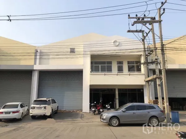工厂 出租在Khlong Luang, Pathum Thani - 两层工厂外立面，配多道卷帘门、玻璃办公区与停车位。