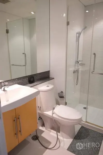 Condominium for rent in Watthana, Bangkok - Modern bathroom with glass-enclosed shower, vanity and crisp white tiling.