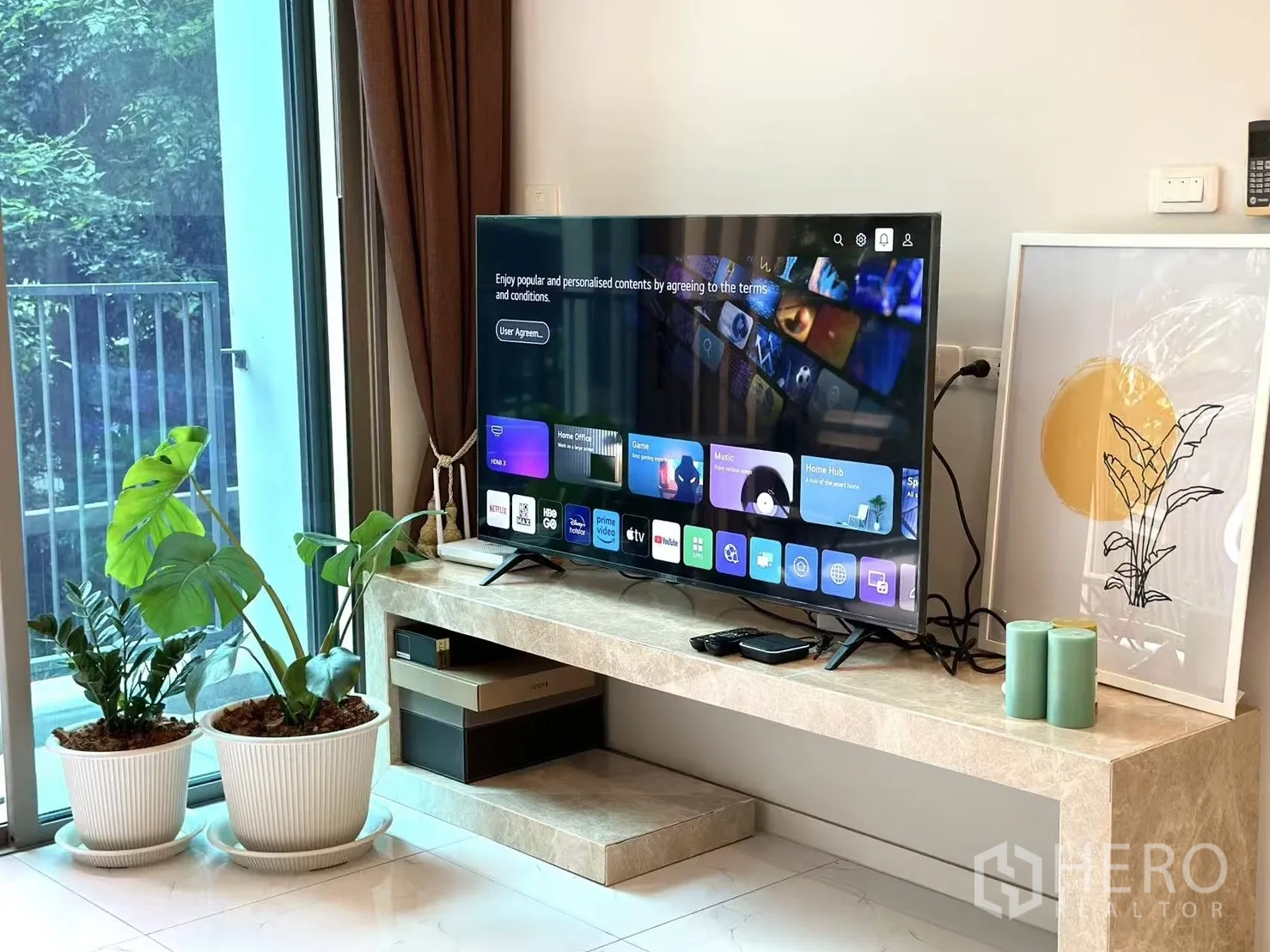 คอนโด ขายในWatthana, Bangkok - มุมห้องนั่งเล่นมีชั้นวางทีวีสมาร์ทและกระถางต้นไม้ข้างประตูกระจก