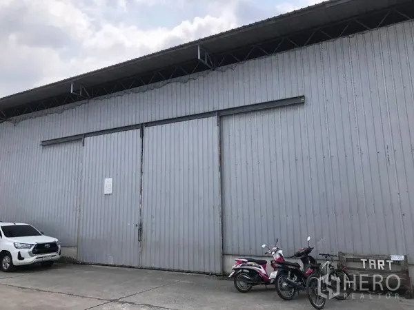 货栈 出租在Pak Kret, Nonthaburi - 金属板外墙的仓库外立面，超大滑动门与现场停车位，位于Pak Kret。
