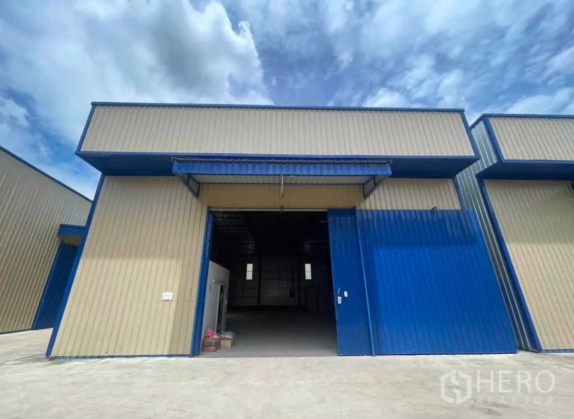 Warehouse for rent in Wang Thonglang, Bangkok - Front view of a warehouse unit with a wide sliding door partly open and a concrete loading area.