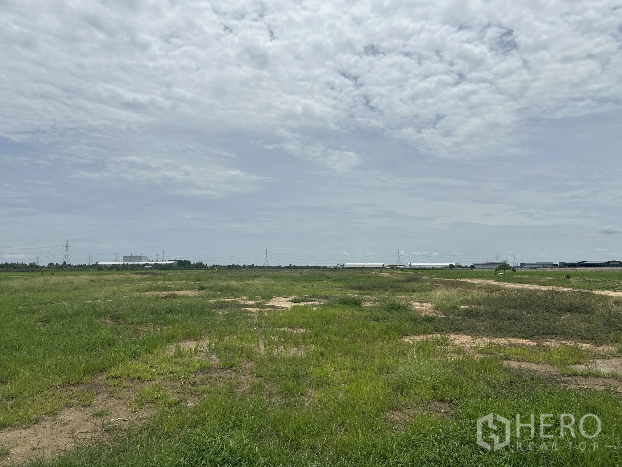 Land for sale in Sai Noi, Nonthaburi - Open, flat field ready for development with warehouses visible in the distance.