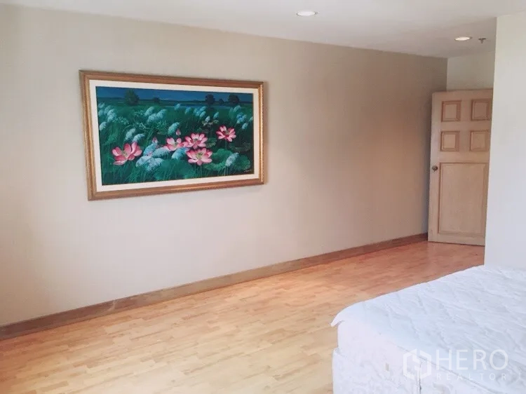 Condominium for rent in Watthana, Bangkok - Cozy bedroom wall with lotus painting and partial bed on wooden flooring.