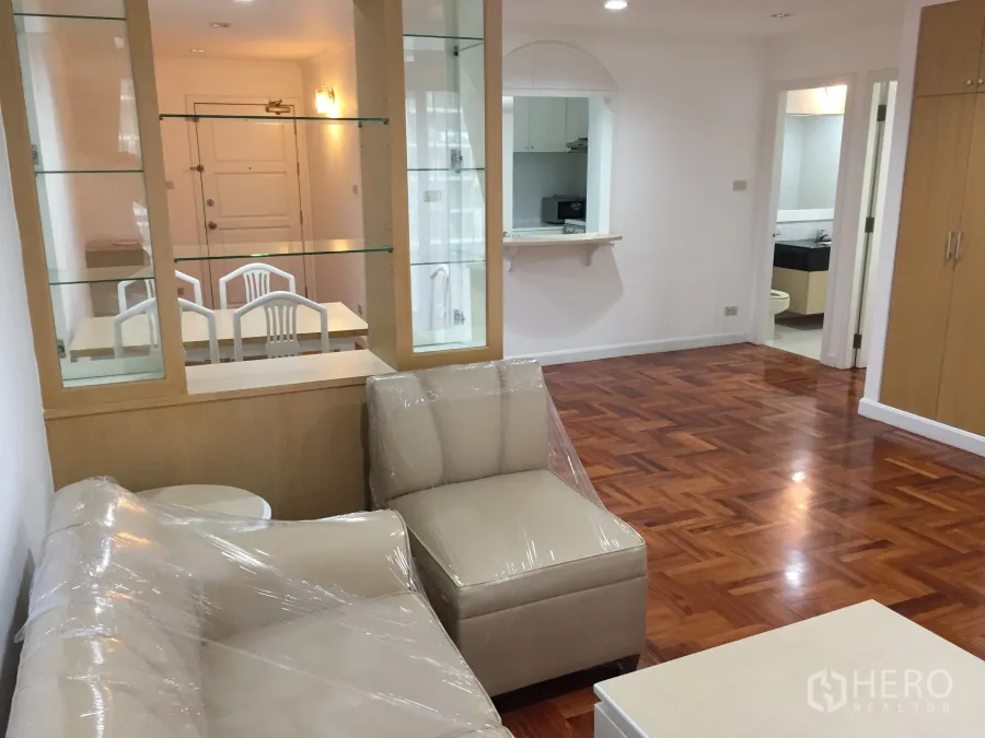 คอนโด ให้เช่าในWatthana, Bangkok - ห้องนั่งเล่นสว่างด้วยตู้โชว์กระจกกั้นโซน โซฟาสีครีม และพื้นปาร์เกต์เงางามต่อเนื่องถึงประตูและห้องน้ำ