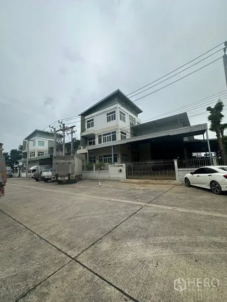 คลังสินค้า ให้เช่าหรือขายในLam Luk Ka, Pathum Thani - มุมมองถนนหน้าโกดังสูง 3 ชั้น พร้อมลานโหลดและรั้วหน้าบ้าน รถบรรทุกจอดริมทาง