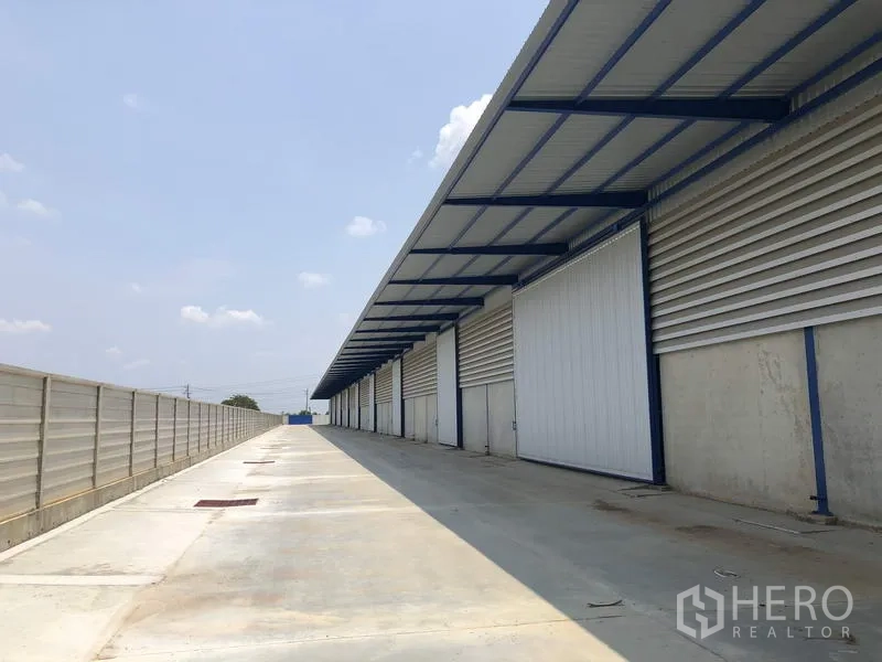 Factory for rent or sale in Lat Lum Kaeo, Pathum Thani - Rear service road along the factory with continuous canopy and multiple sliding doors.