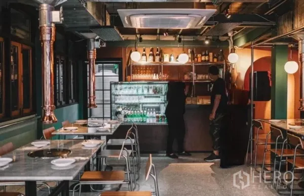 บ้าน ขายในKhlong Toei, Bangkok - มุมบาร์พร้อมตู้แช่เครื่องดื่ม ชั้นวาง และไฟสมัยใหม่ ถัดจากโต๊ะทานอาหารที่จัดเรียงเป็นระเบียบ