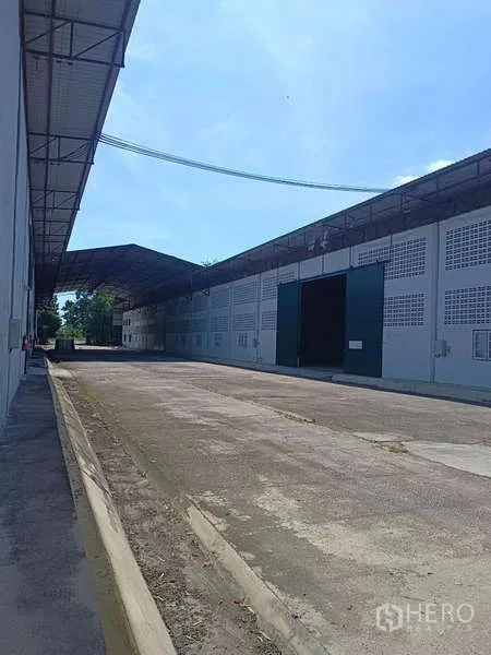 货栈 出租在Mueang Rayong, Rayong - 外部装卸通道，长条仓库立面与绿色滑动大门。