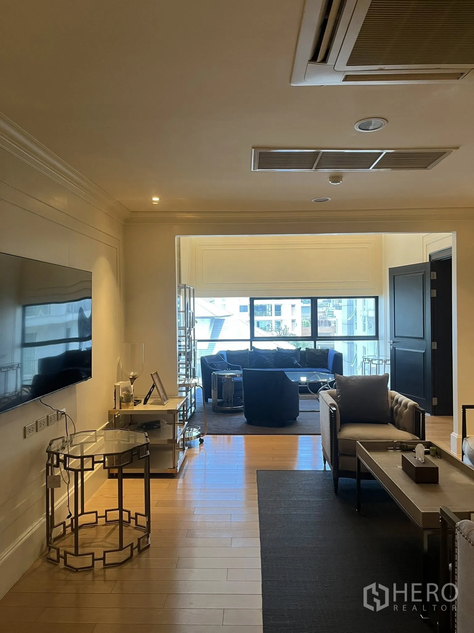 Home Office for rent in Watthana, Bangkok - Living area with TV, sofas, and a large window leading to a lounge.