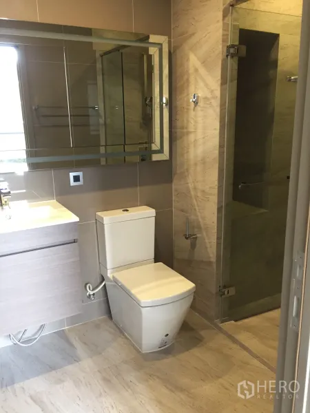 Condominium for rent in Watthana, Bangkok - Modern bathroom with large mirror, vanity, and glass-enclosed walk-in shower.
