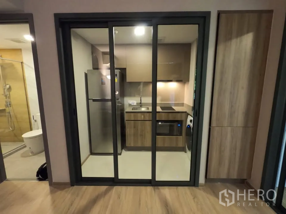 Condominium for rent in Watthana, Bangkok - Kitchen seen through three-panel glass doors, bathroom entrance to the left.