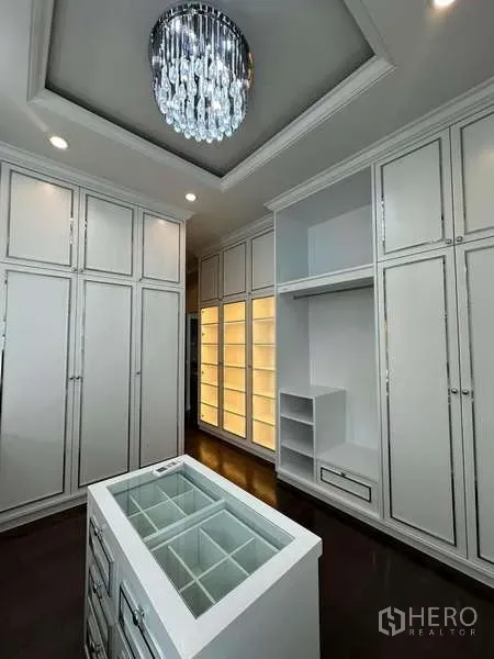 独立式住宅 出售在Prawet, Bangkok - 步入式衣帽间，白色定制柜、玻璃台岛与水晶吊灯。