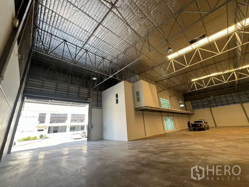 货栈 出租在Prawet, Bangkok - 带夹层办公室的仓库大厅，装卸门开启，内有车辆。