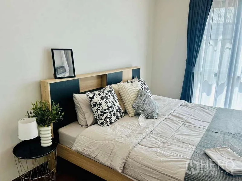 Detached House for rent in Bang Phli, Samut Prakan - Cozy guest bedroom with large bed, side table and blue drapes opening to a balcony door.