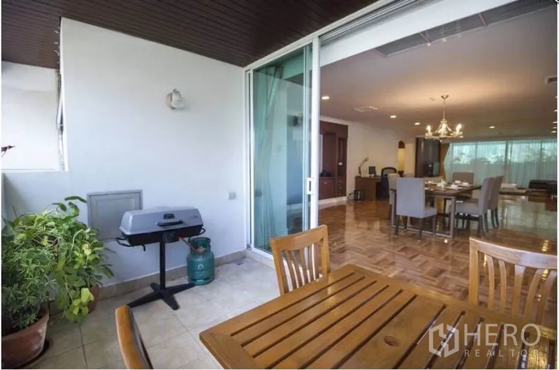 อพาร์ทเมนท์ ให้เช่าในRatchathewi, Bangkok - ระเบียงมีหลังคาพร้อมโต๊ะไม้ กระถางต้นไม้ และเตาย่างแก๊ส ถัดจากประตูกระจกสไลด์สู่พื้นที่นั่งเล่นแบบเปิด