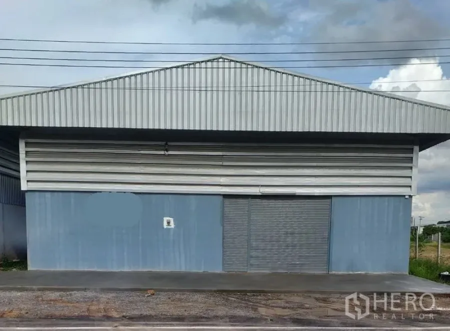 คลังสินค้า ให้เช่าในBang Yai, Nonthaburi - ด้านหน้าตัวอาคารหลังคาทรงจั่วเมทัลชีท ประตูม้วนขนาดใหญ่ และทางเท้าคอนกรีต