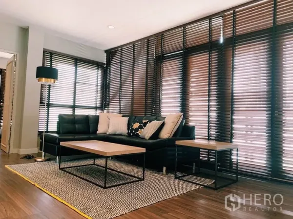 公寓 出租在Watthana, Bangkok - 舒适起居区，L形皮沙发、茶几、地毯与层次百叶。