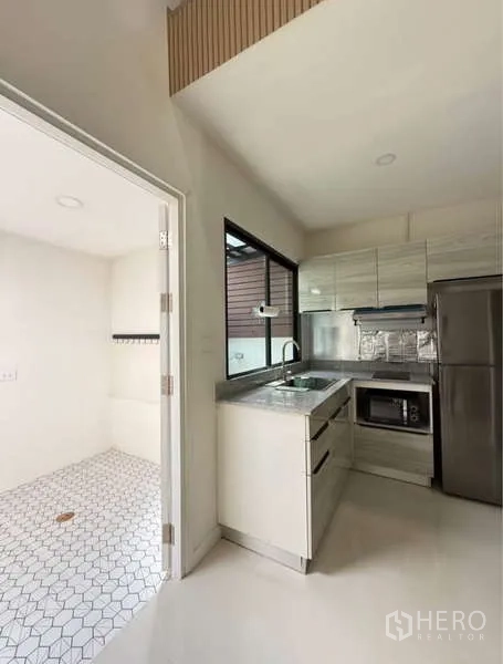 联排别墅 出租在Bang Phli, Samut Prakan - 现代L形厨房，白色橱柜与不锈钢电器，旁连洗衣区。