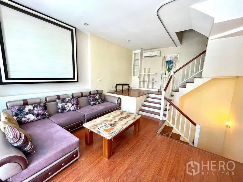 Townhouse for rent in Saphan Sung, Bangkok - Bright living room with sectional sofa, coffee table and steps to a raised platform area.