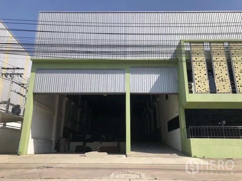โรงงาน ขายในBang Phli, Samut Prakan - ด้านหน้าโรงงานติดถนน โครงสร้างสีเขียว ประตูม้วนคู่ เพดานสูง และทางรถเข้าออกกว้างในย่านบางพลี