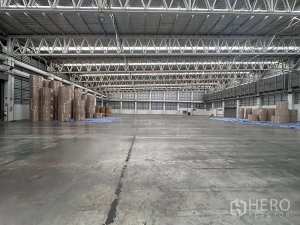 โรงงาน ให้เช่า - พื้นโกดังกว้าง หลังคาโครงถักเหล็กมีช่องแสง และกองม้วนกระดาษด้านข้าง