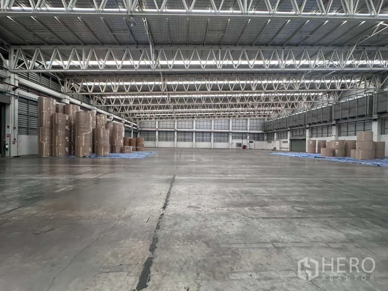 โรงงาน ให้เช่า - พื้นโกดังกว้าง หลังคาโครงถักเหล็กมีช่องแสง และกองม้วนกระดาษด้านข้าง