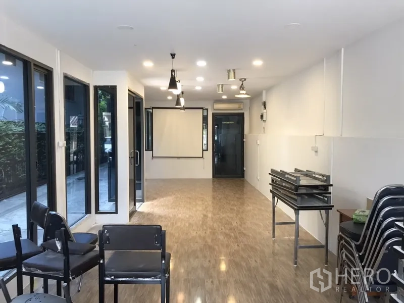 零售空间 出租在Watthana, Bangkok - 明亮的开间店铺，木纹地面、筒灯与吊灯，落地窗与投影幕一应俱全。