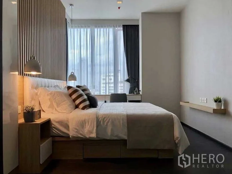 Condominium for rent in Watthana, Bangkok - Modern bedroom with queen bed, slatted wood headboard, pendant lamps and a desk by a floor‑to‑ceiling window.