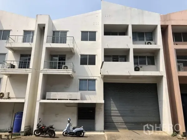 工厂 出租或出售在Khlong Luang, Pathum Thani - 白色多层厂房外立面，带大卷闸门、阳台与空调外机，临路而建
