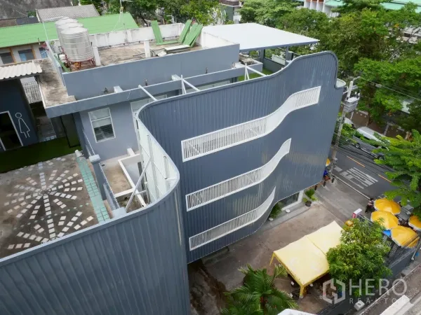 独立商业地产 出租在Bang Rak, Bangkok - 俯瞰现代独栋建筑，弧形金属外立面、外置白色楼梯与树荫前庭，位于邦拉区。