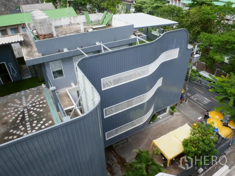 独立商业地产 出租在Bang Rak, Bangkok - 俯瞰现代独栋建筑，弧形金属外立面、外置白色楼梯与树荫前庭，位于邦拉区。