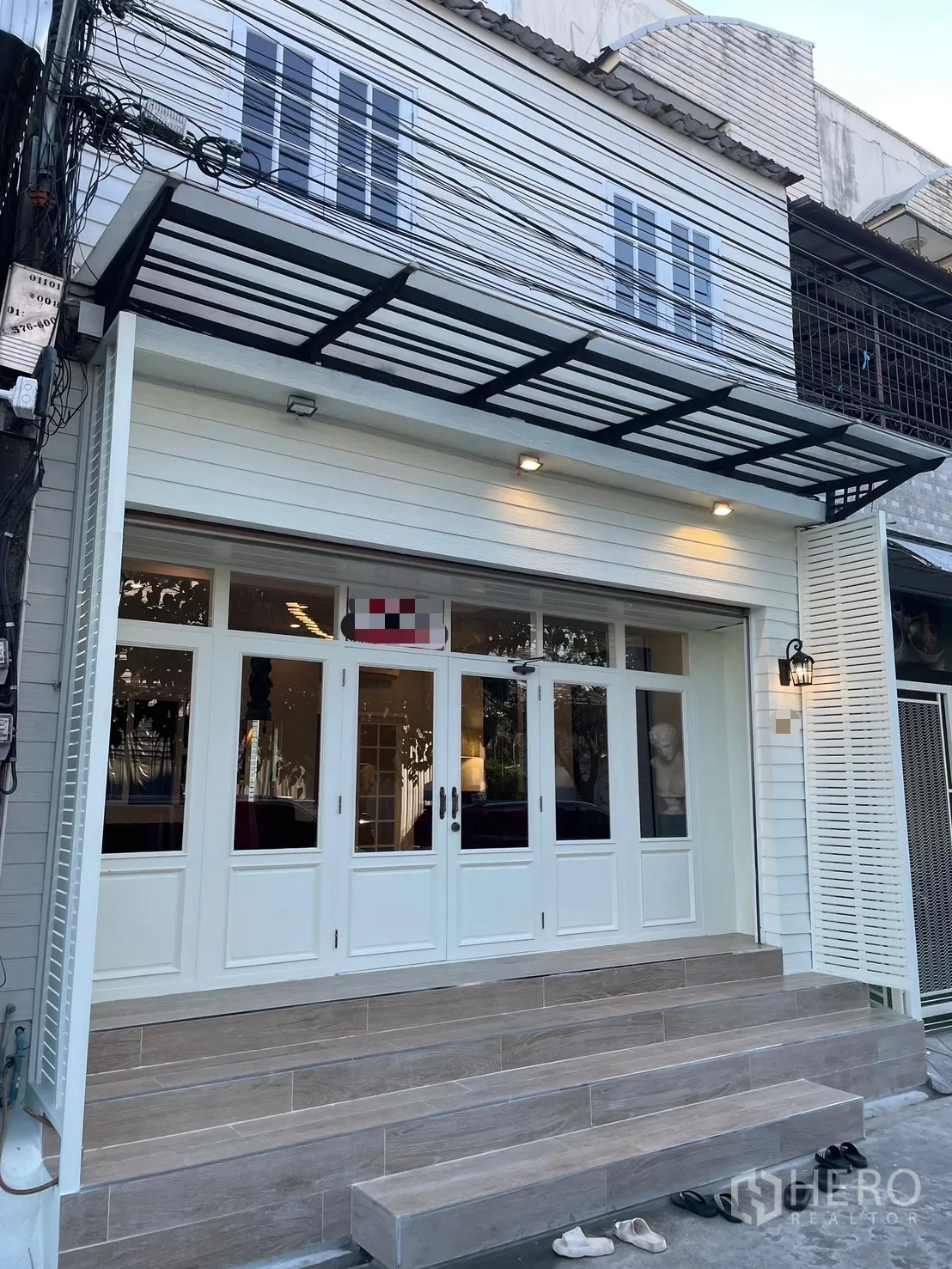 Shophouse for rent in Bang Kapi, Bangkok - Shophouse exterior with white facade, glass‑panel doors, metal awning and wide steps.