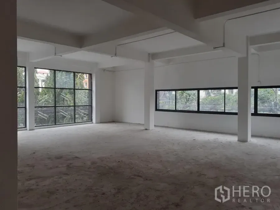 Office Space for rent in Khlong Toei, Bangkok - Unfurnished open-plan office floor with white columns, exposed conduits and large black-framed windows overlooking greenery in Phra Khanong, Bangkok.