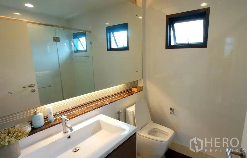 Detached House for rent in Bang Kapi, Bangkok - Contemporary bathroom with glass-enclosed shower, wide vanity, mirror and window.