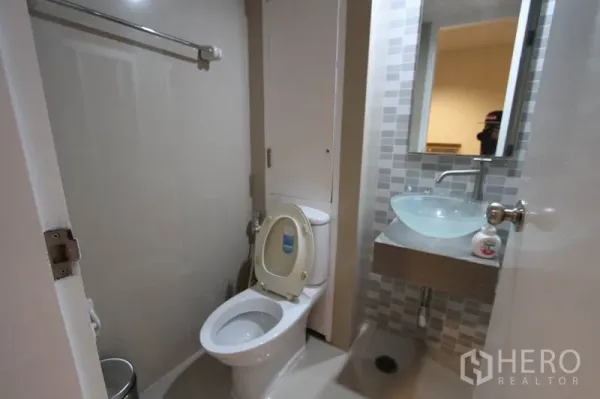 Condominium for rent or sale in Wang Thonglang, Bangkok - Bathroom with toilet, glass vessel sink, and tiled vanity wall under a mirror.