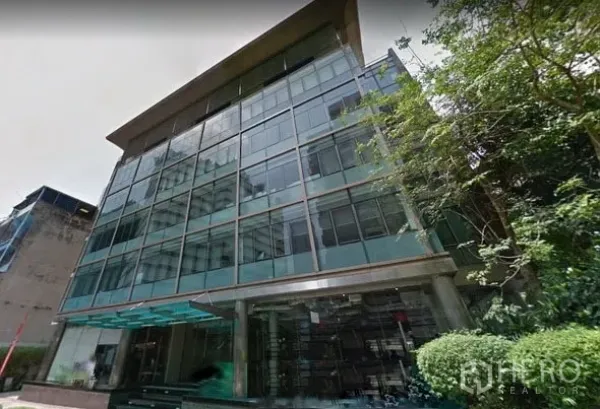 Office Space for rent in Khlong Toei, Bangkok - Modern glass-fronted office building exterior with reflective facade, entrance canopy, and landscaped greenery in Bangkok.
