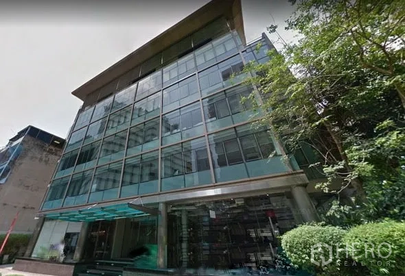 Office Space for rent in Khlong Toei, Bangkok - Modern glass-fronted office building exterior with reflective facade, entrance canopy, and landscaped greenery in Bangkok.
