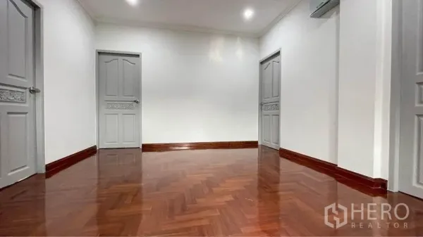 Detached House for rent in Bang Kapi, Bangkok - Bright upstairs landing with herringbone wood floor, white walls and three gray paneled doors.