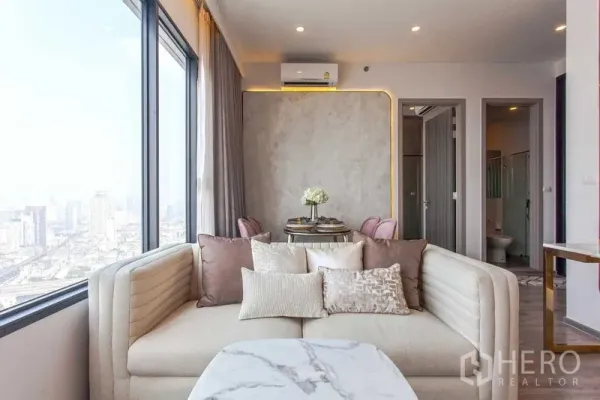 Condominium for rent in Watthana, Bangkok - Cozy corner sofa with plush cushions facing large windows and city views, with doors to bedrooms and bathrooms.
