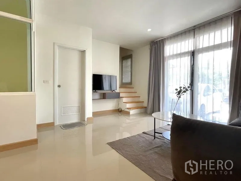 Townhouse for rent in Bang Phli, Samut Prakan - Ground-floor living space with TV wall, sliding glass doors and steps to the upper floor.