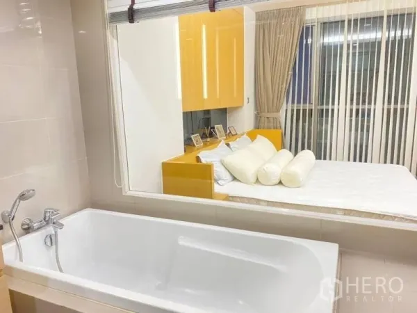 คอนโด ให้เช่าในWatthana, Bangkok - อ่างอาบน้ำสีขาวกับผนังกระจกมองเห็นห้องนอนอบอุ่นที่มีมู่ลี่