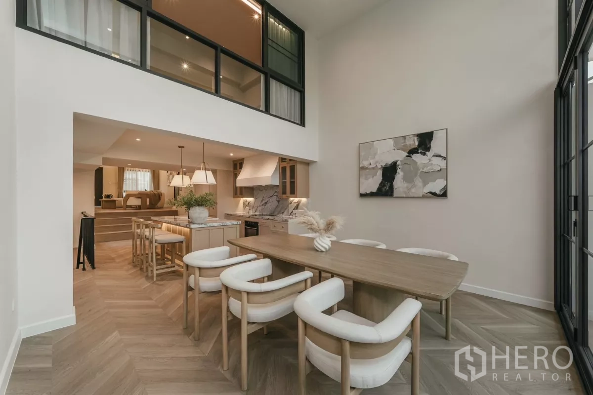 联排别墅 出租在Watthana, Bangkok - 餐厅挑高空间，挂画与夹层窗户俯瞰厨房。