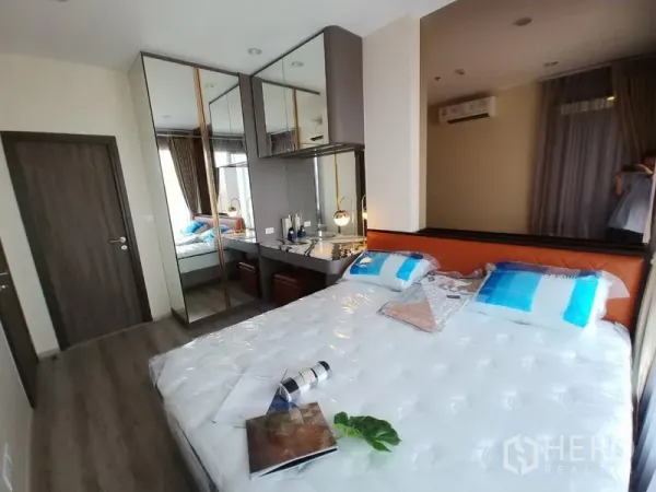 Condominium for rent in Huai Khwang, Bangkok - Bright bedroom with queen bed, mirrored wardrobes, dressing desk, and large window.